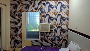 Ein Zimmer mit einem gemusterten Wandbild, einem Fenster und einer Klimaanlage.