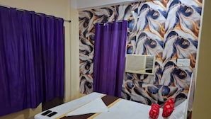 Ein Hotelzimmer mit Bett, violetten Vorhängen, einer Wandklimaanlage und einem gemusterten Wandteppich.