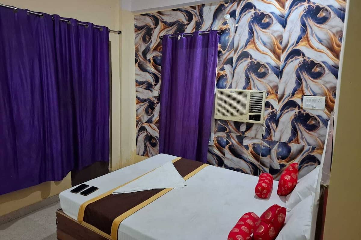 Hotellihuone, jossa on sänky, violetit verhot, seinään asennettu ilmastointilaite ja kuviollinen tapetti.