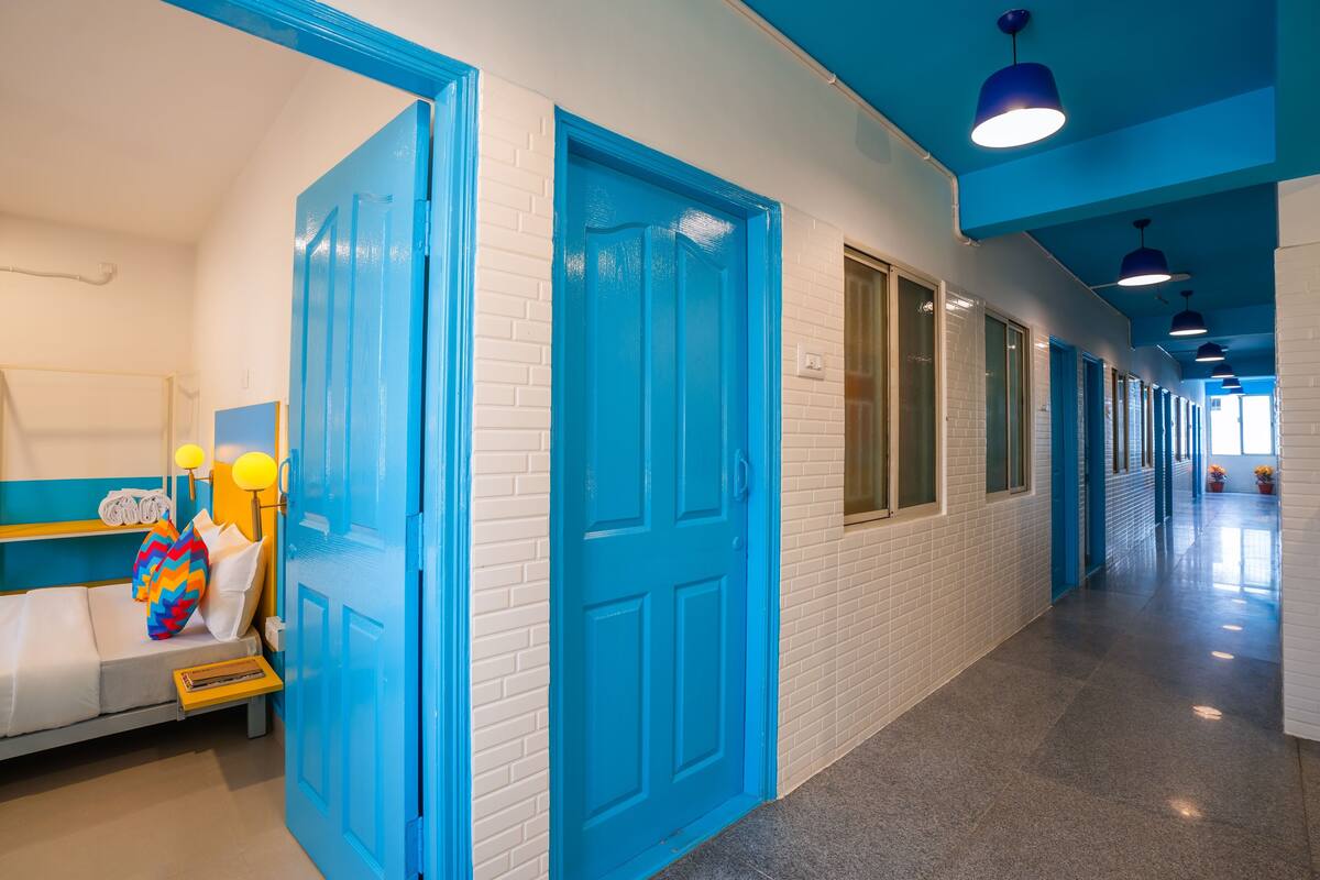 A hotel corridor with blue doors, a bed with pillows, and a bench.