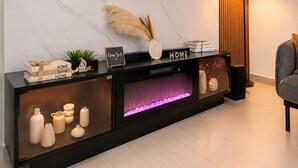 Un salon moderne avec un téléviseur à écran plat fixé à un mur en marbre, une console en bois agrémentée d’objets décoratifs, une cheminée et une lampe.