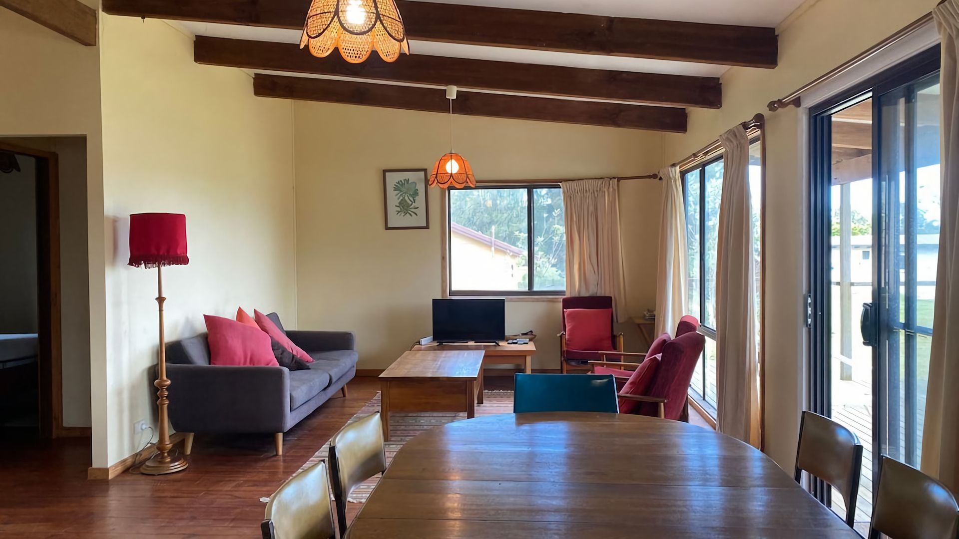 A living room with a sofa, a table, chairs, a television, and large windows.