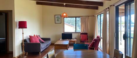 A living room with a sofa, a table, chairs, a television, and large windows.