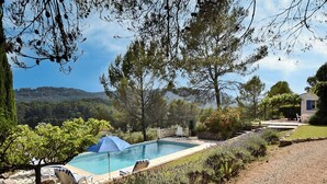 Ein Schwimmbad mit Liegestühlen, umgeben von einem angelegten Garten und Blick auf Hügel.