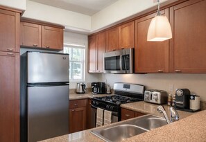 A modern kitchen with stainless steel appliances, wooden cabinets, granite countertops, and a pendant light. - DS1 BR Getaway In MDR (Marina del Rey)