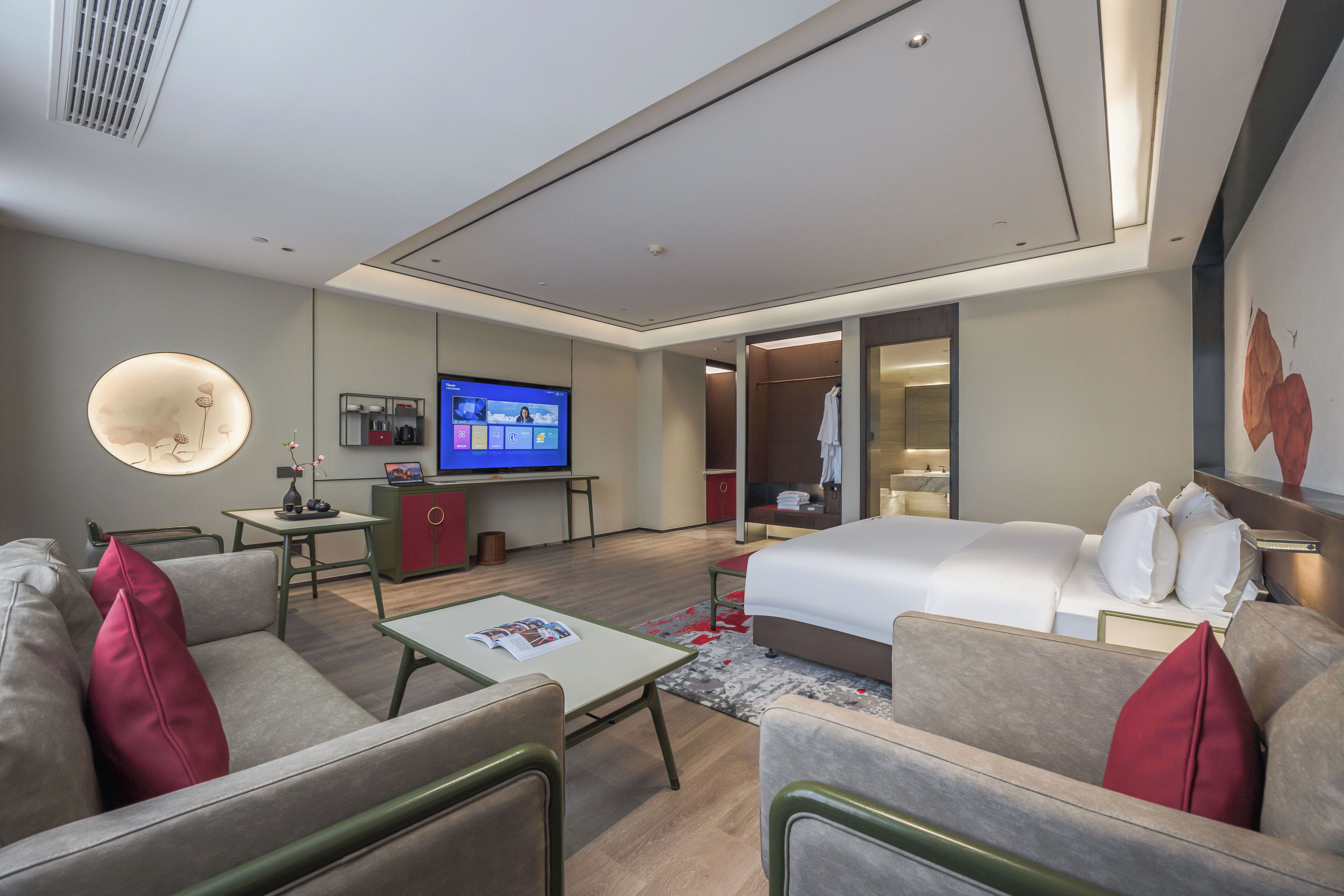Une chambre d’hôtel moderne équipée d’un lit, d’un coin salon, d’une télévision et d’une salle de bain visible à travers une porte ouverte.