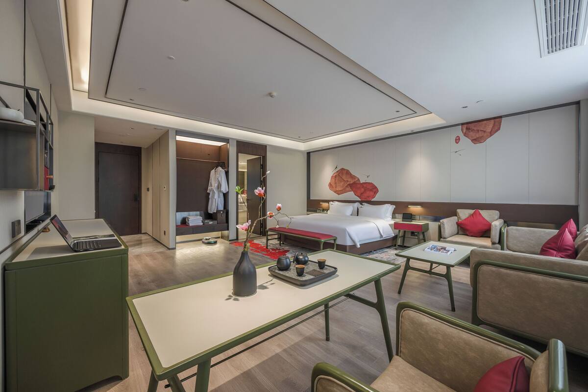 A modern hotel room with a bed, seating area, and a desk with a laptop.