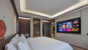 Une chambre d’hôtel moderne dotée d’un grand lit, d’un téléviseur à écran plat proposant une sélection de films et d’un design minimaliste.