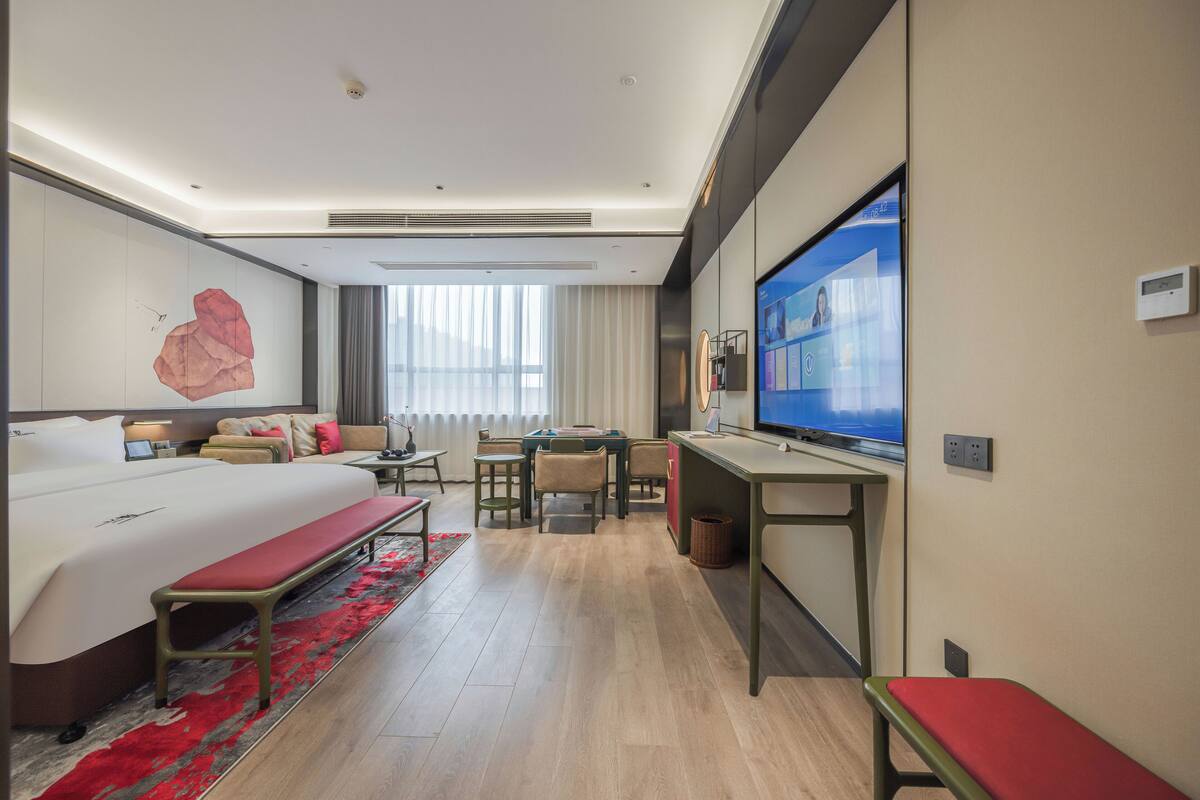 A modern hotel room with a large bed, a desk, a television, and a seating area.