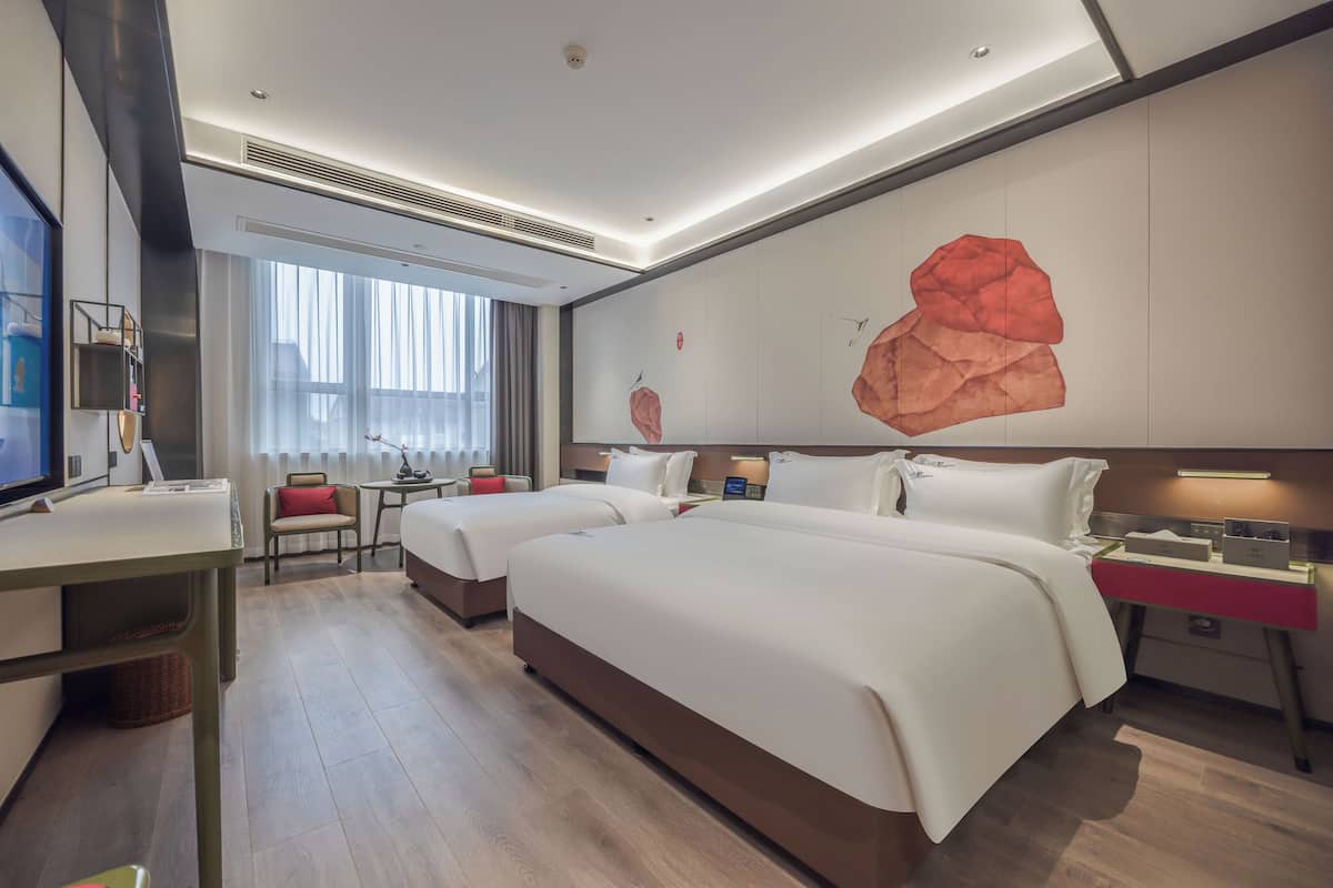 A hotel room with two beds, a desk, a chair, a TV, and a large abstract painting on the wall.