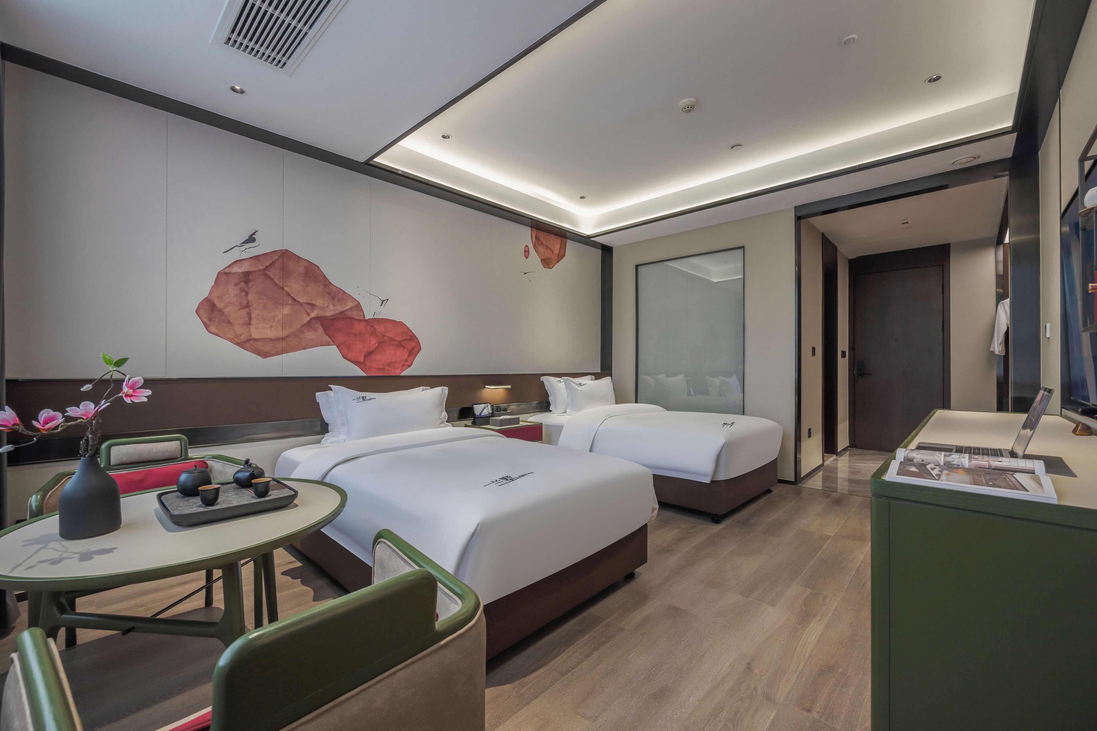 A modern hotel room with two beds, a desk, a vase with flowers, and a wall mural.