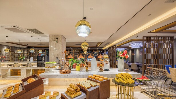 Un hall d'hôtel avec un espace buffet proposant du pain, des viennoiseries et des fruits.