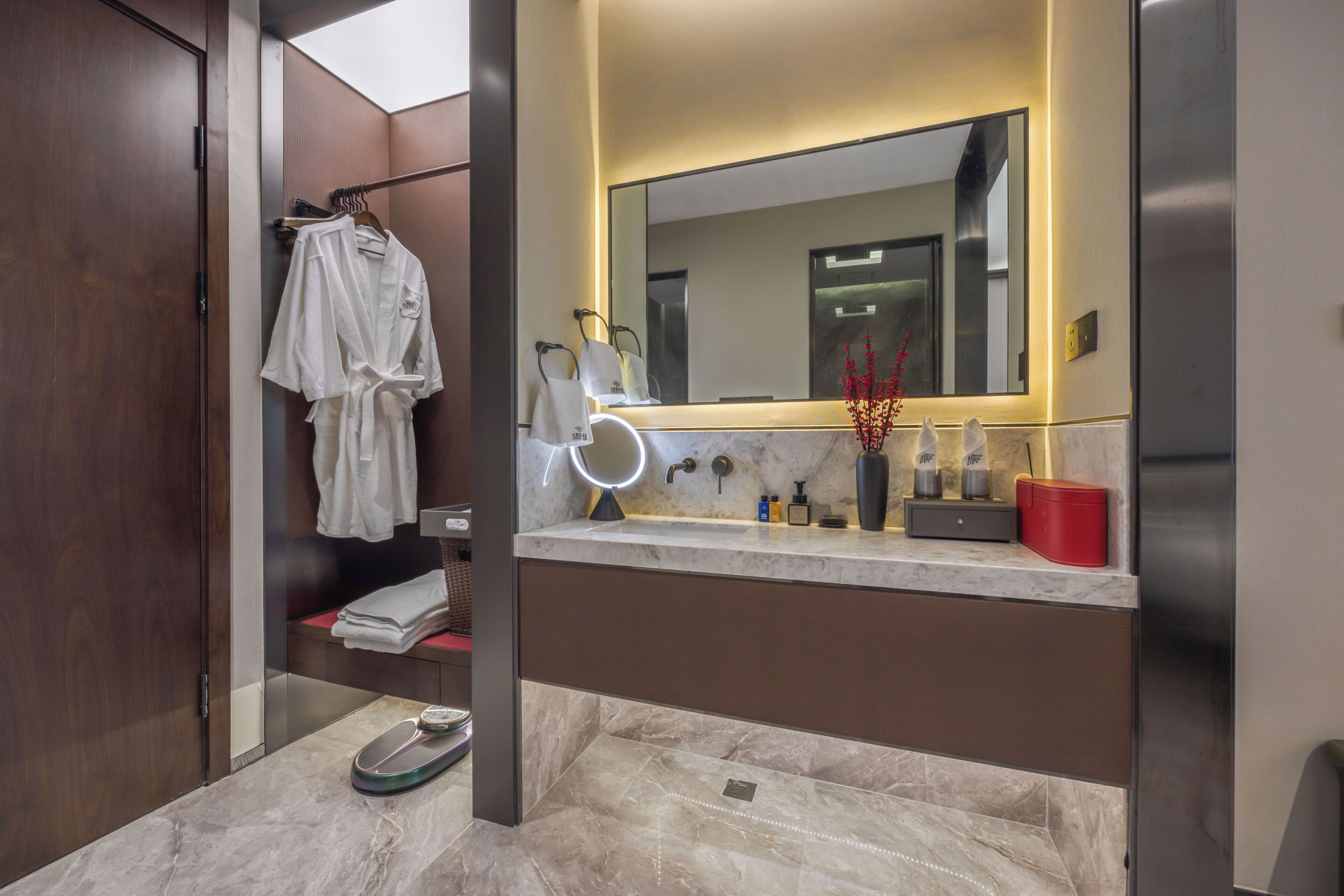 Un bagno moderno con un vanità in marmo, un grande specchio e una scatola portaoggetti rossa.