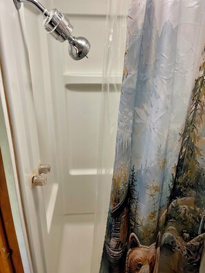 A bathroom with a shower curtain featuring a bear design, a white door, and a showerhead.