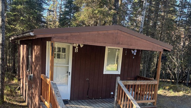 A small wooden cabin with a front door, a window, and a wooden staircase leading to a porch. - Cozy Studio Cabin in Kasilof – Comfort Close to Nature (Kasilof)