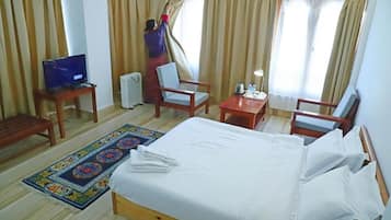 Habitación de hotel con cama, dos sillas, una mesita, televisor y ventana con cortinas en ajuste.