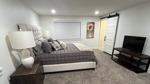 Un dormitorio con cama, televisor, cómoda y ventana con persianas.