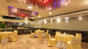 A banquet hall with round tables and chairs, a bar area, and a seating section. - First By JPM (New Delhi)