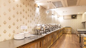 A buffet setup with multiple serving stations, a wooden floor, and patterned wallpaper. - First By JPM (New Delhi)