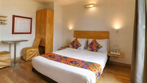 A hotel room with a bed, a desk, a chair, and a wardrobe. - First By JPM (New Delhi)
