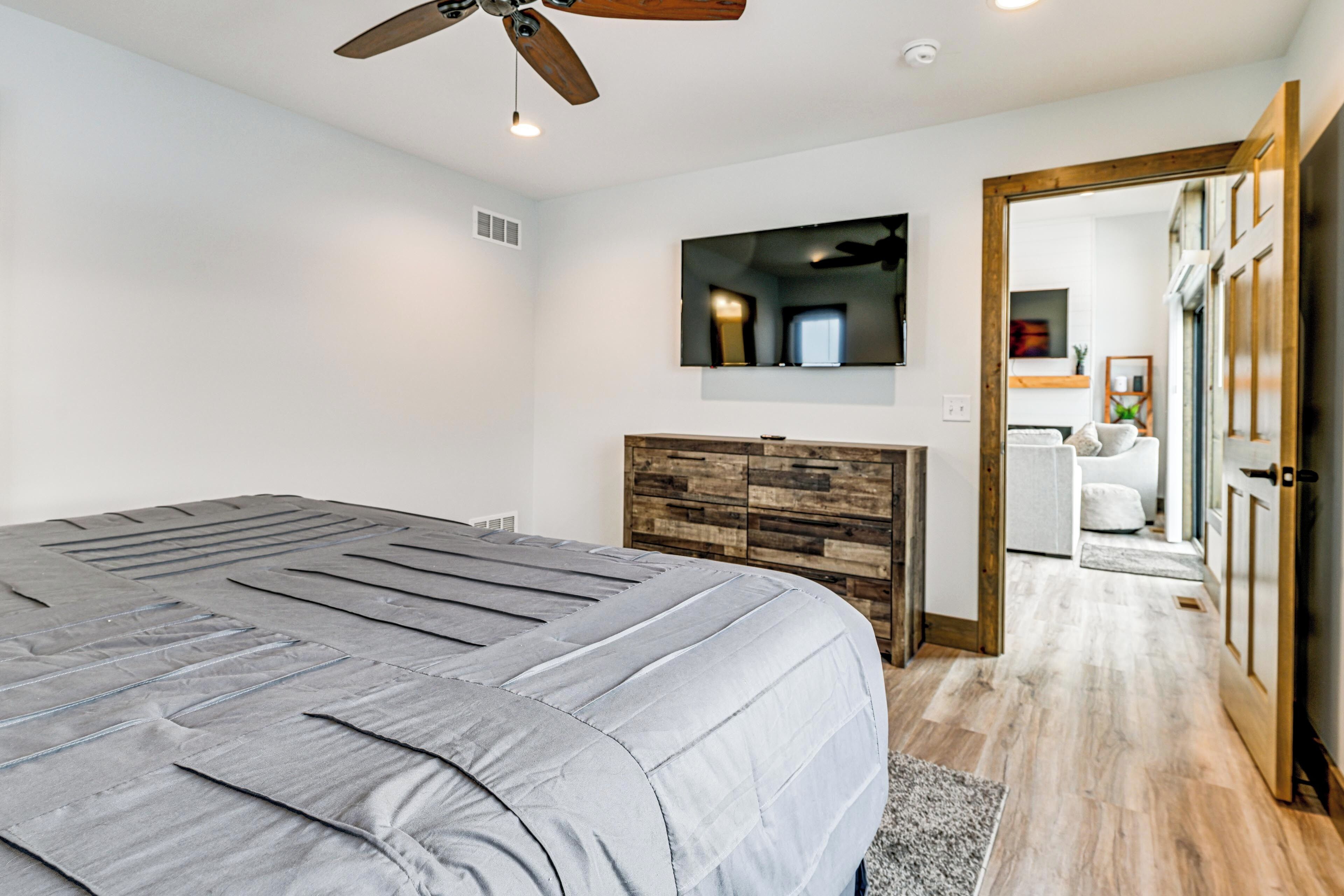 A bedroom with a large bed, a wooden headboard, a ceiling fan, and a TV mounted on the wall.