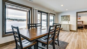 Un comedor con mesa y sillas de madera, ventanas amplias con vistas a un paisaje nevado, y un cuadro en la pared.
