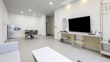 A modern hotel room with a large flat-screen TV, a dining area with a table and chairs, a kitchenette, and a seating area with a sofa and a small table.