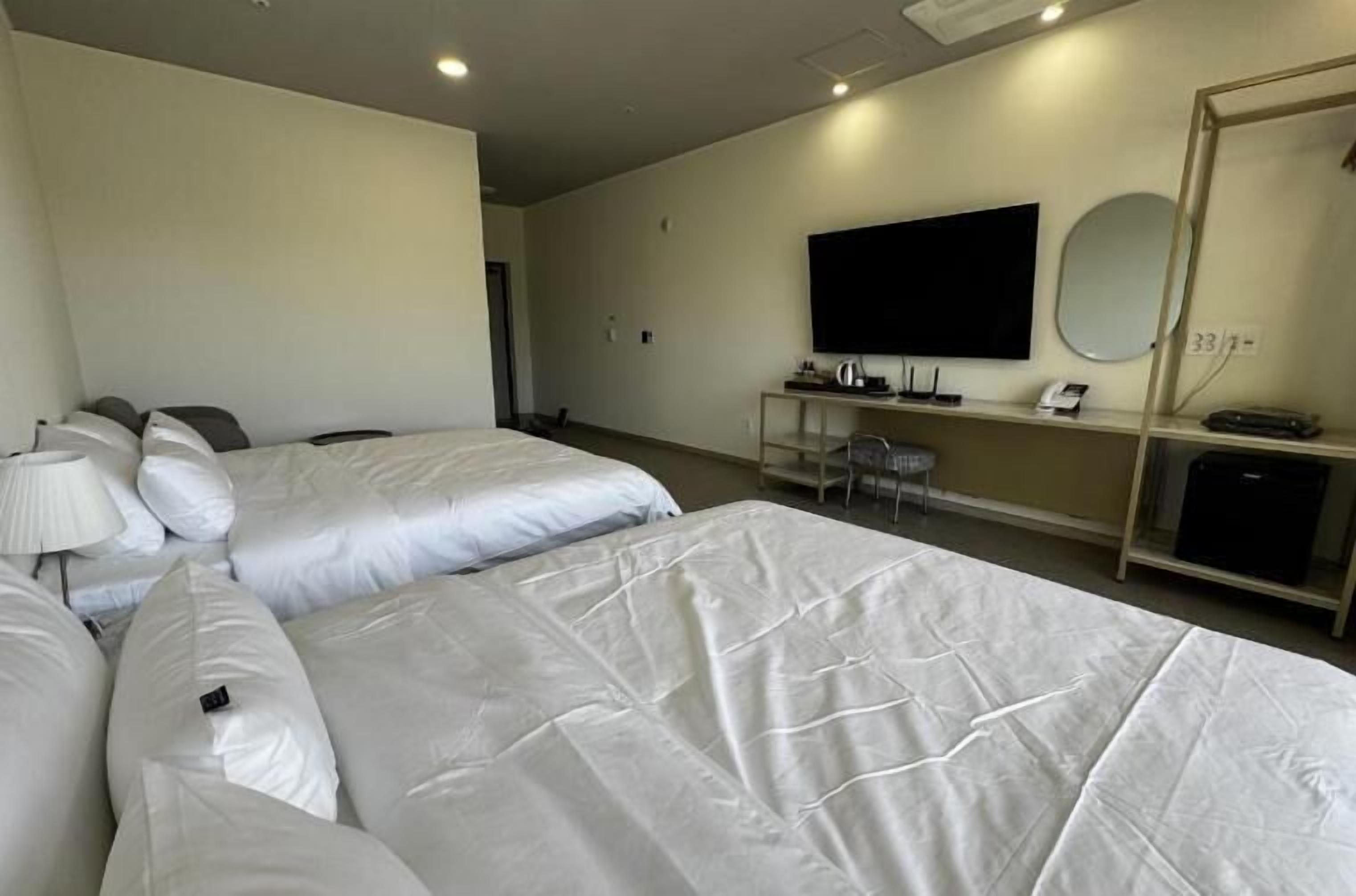 Habitación de hotel con dos camas, un escritorio, un televisor de pantalla plana, un espejo y una estantería con tetera y teléfono.