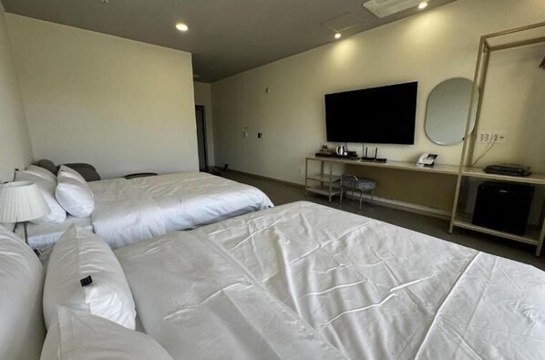 A hotel room with two beds, a desk with a flat-screen TV, a mirror, and a shelf with a kettle and phone. - Mokpo Centum Tourist Hotel Nam-ak Branch (Muan)