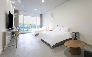 A hotel room with two beds, a desk with a TV, a small table, and a balcony with a view.