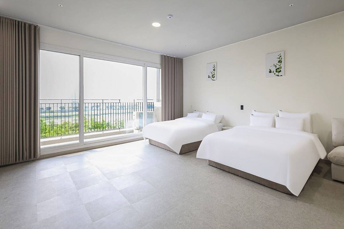 A hotel room with two beds, a large window with a view, and a balcony.