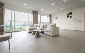 A modern living room with a sectional sofa, a coffee table, and a view of a cityscape through large windows. - Mokpo Centum Tourist Hotel Nam-ak Branch (Muan)