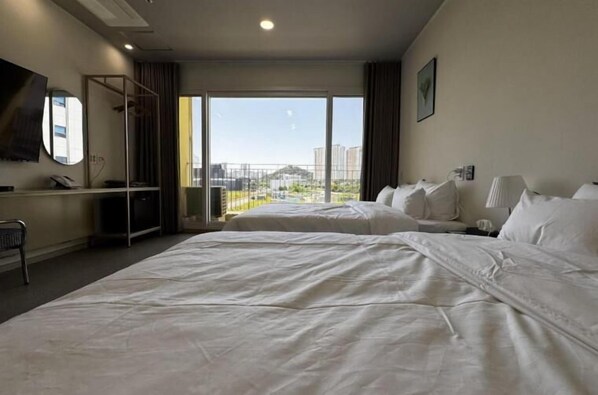 Habitación de hotel con dos camas, un escritorio, una silla, un ventanal grande con vistas a la ciudad y un balcón.