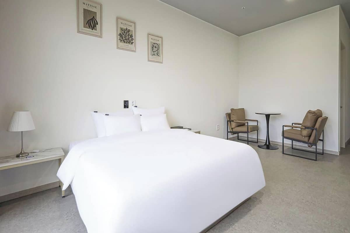 A hotel room with a large bed, two chairs, a small table, and three framed artworks on the wall.