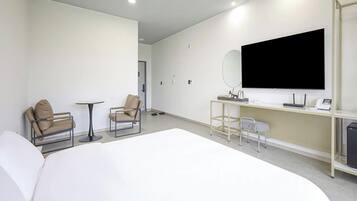 Ett hotellrum med en stor säng, två fåtöljer, ett litet runt bord, ett skrivbord med en dator och en telefon samt en tv som är monterad på väggen.