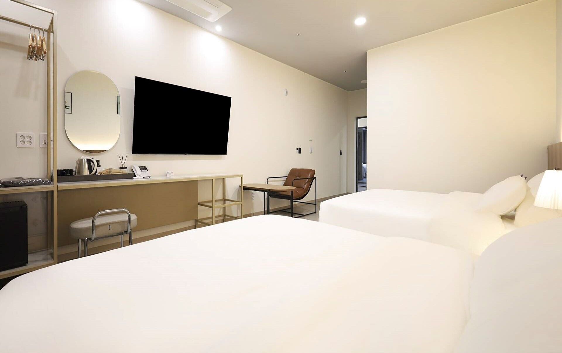 Habitación de hotel con dos camas, un escritorio, un televisor de pantalla plana, una silla y un espejo.