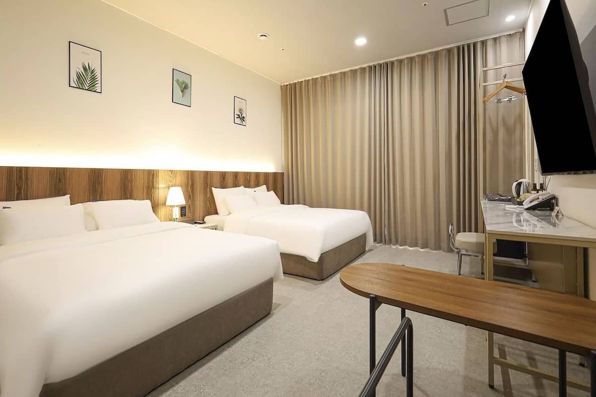 A hotel room with two beds, a desk, a chair, a lamp, and a TV.