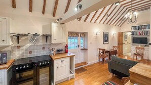 A kitchen with a stove, oven, and white cabinets. There is a dining area with a table, chairs, and a television.