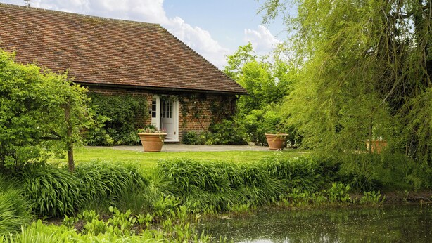 A brick building with a tiled roof, a front door, and a small garden with a pond.