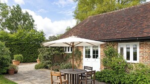 A brick house with a white door, a garden with a patio table and chairs, and a large umbrella.