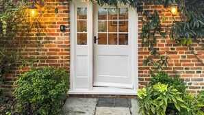 A brick house with a white door, a small porch, and potted plants.
