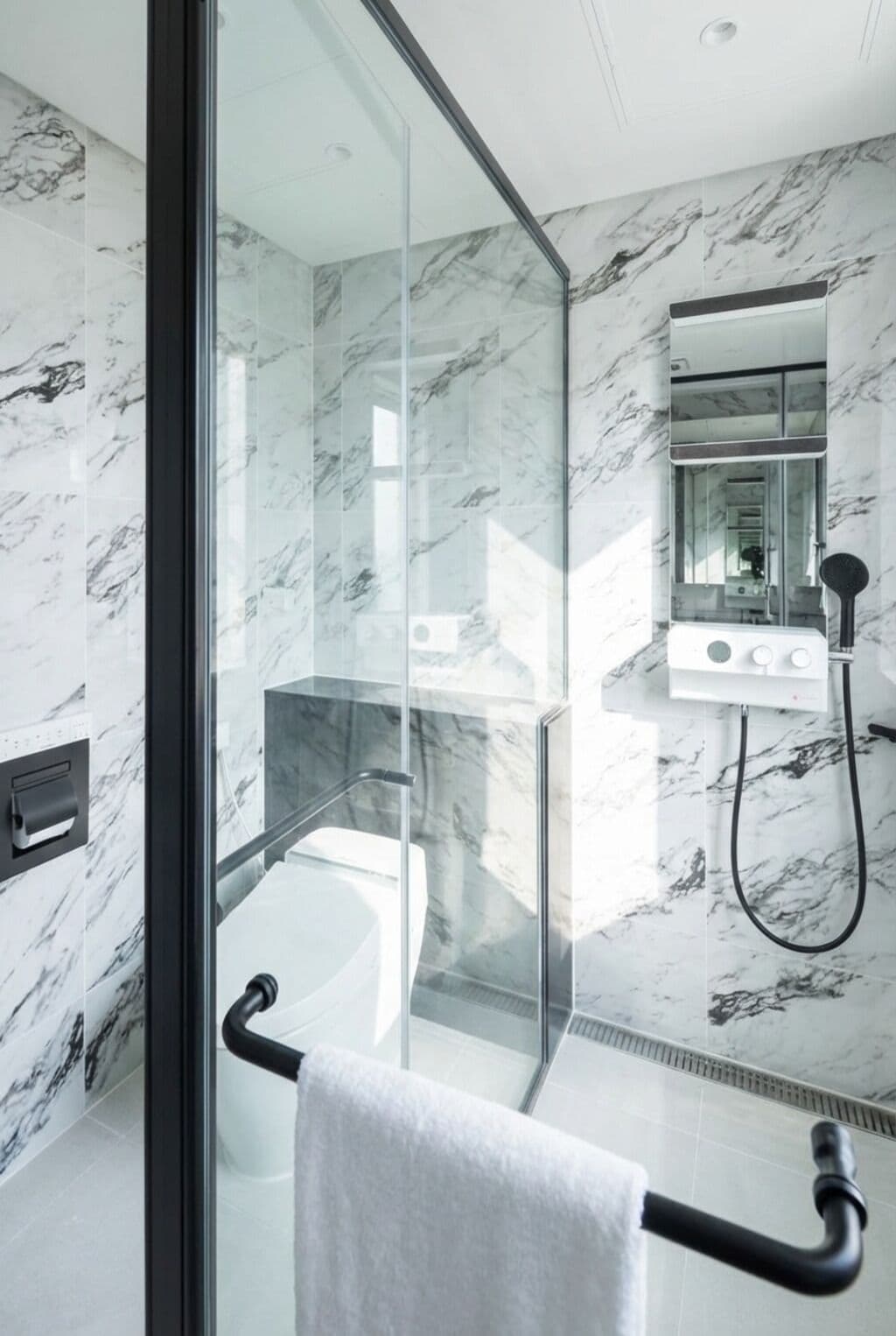 A modern bathroom with a glass shower enclosure, a white bathtub, and a marble-tiled wall.