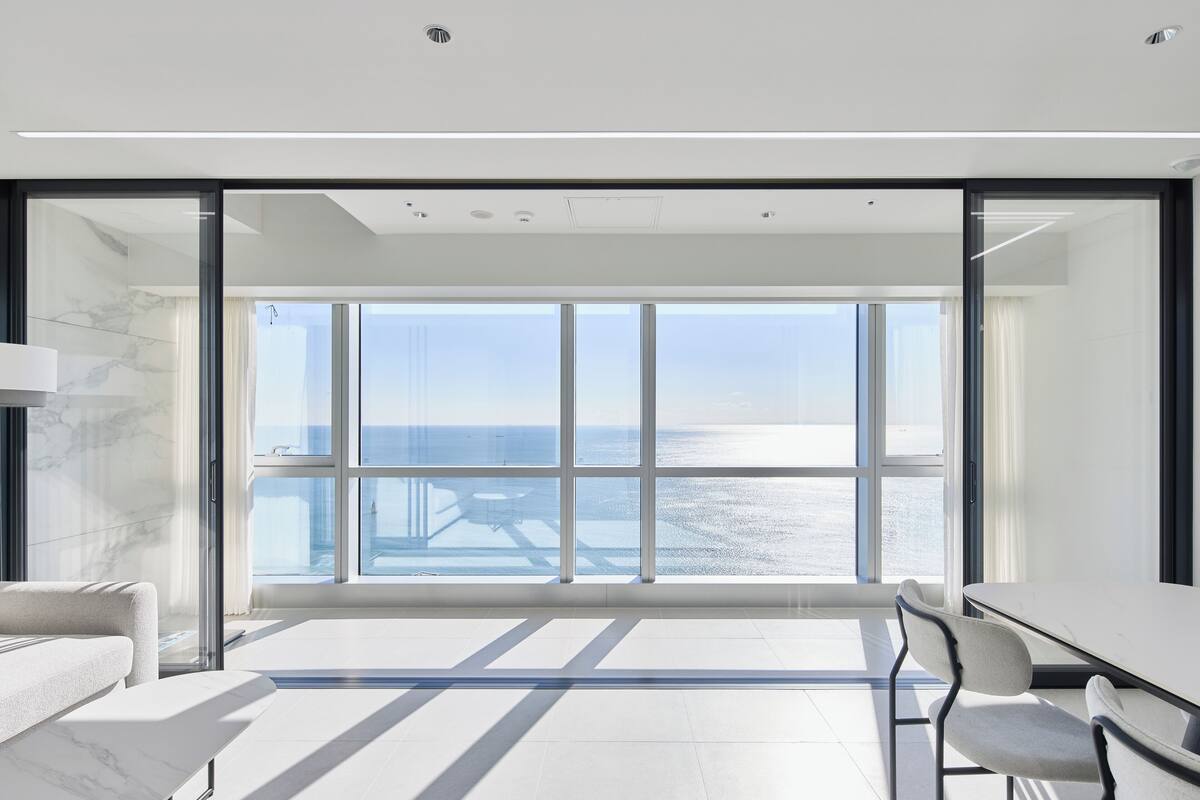 A modern room with a large window, a white sofa, a dining table, and chairs.