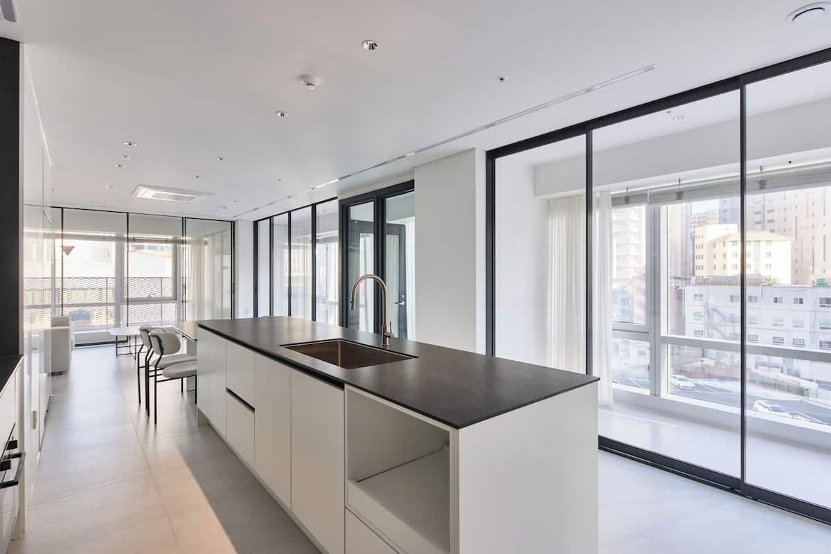 A modern kitchen with a large window, white cabinetry, and a black countertop.