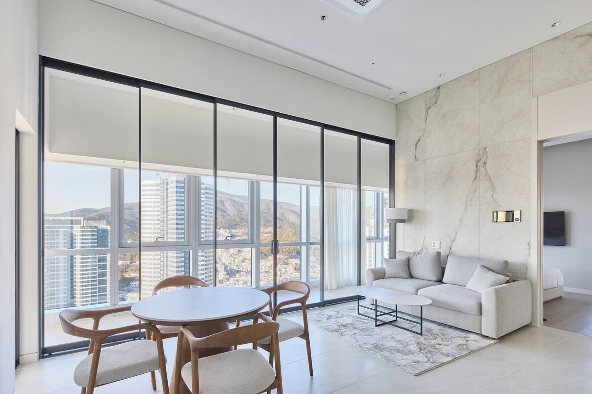 A spacious living room with a large window, a round dining table, and a sofa.