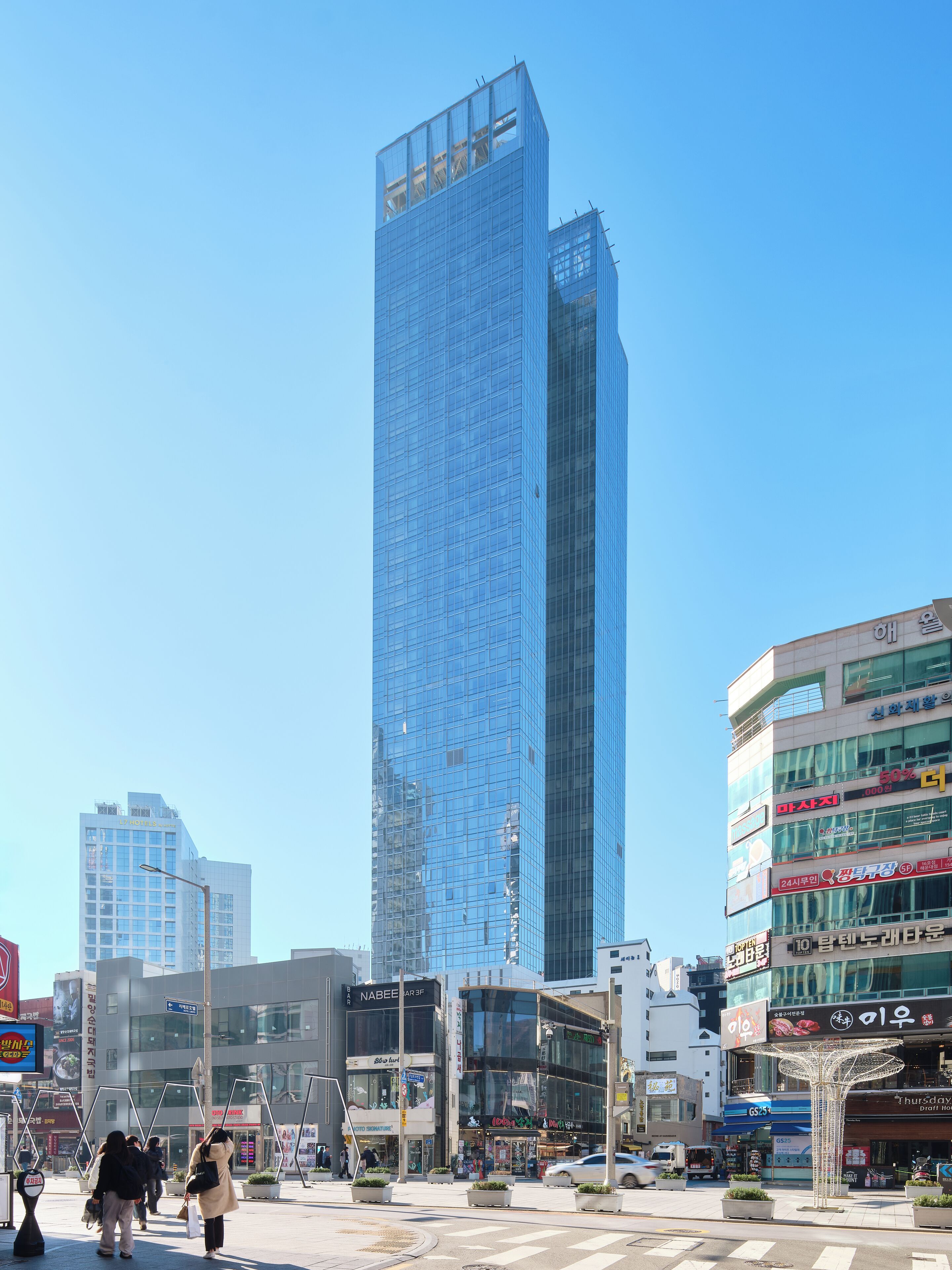 Un moderno edificio de gran altura con fachada de vidrio, rodeado de infraestructura urbana y peatones.
