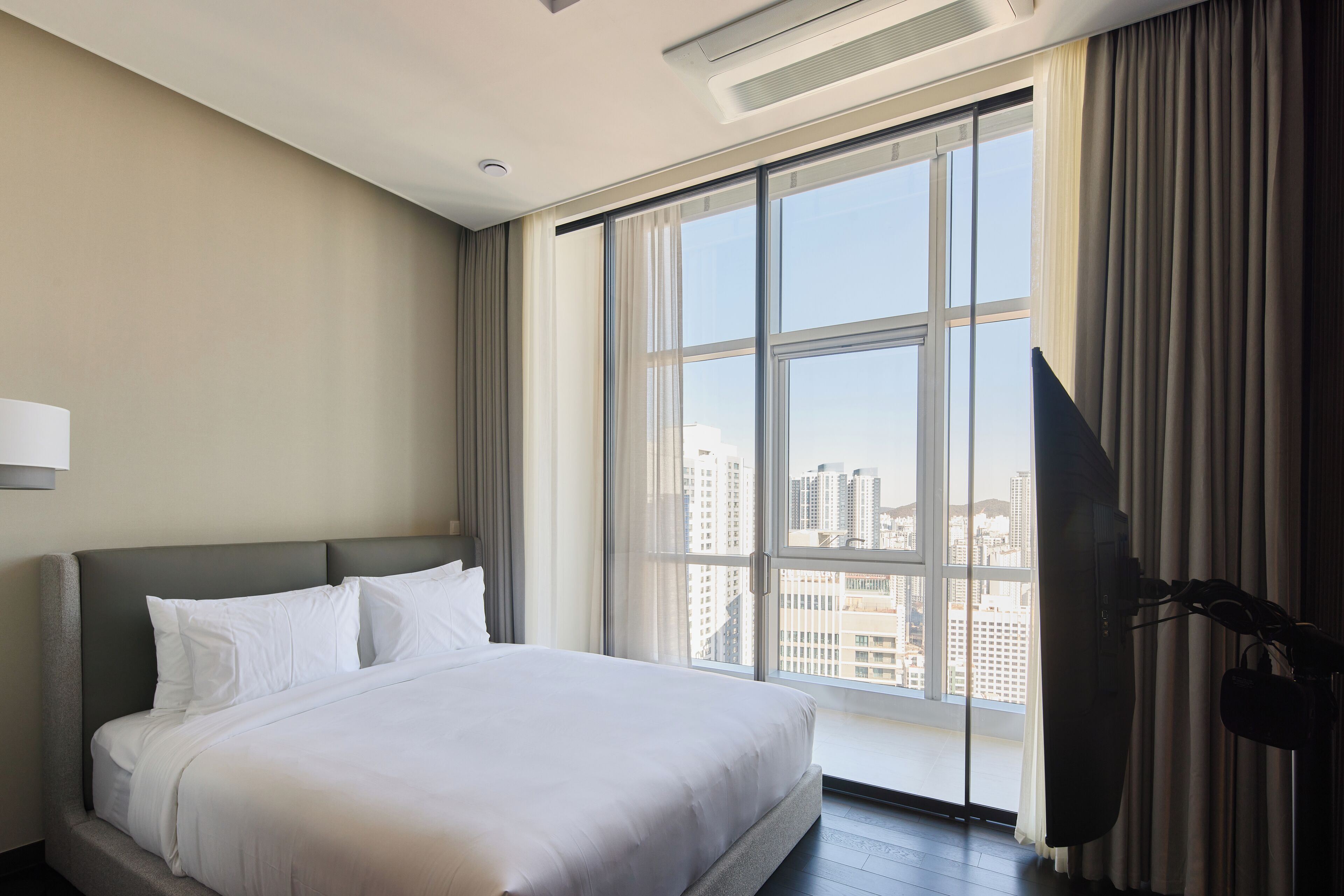 A hotel room with a large bed, a flat-screen TV, and a view of the city through a large window.