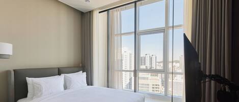 A hotel room with a large bed, a flat-screen TV, and a view of the city through a large window.