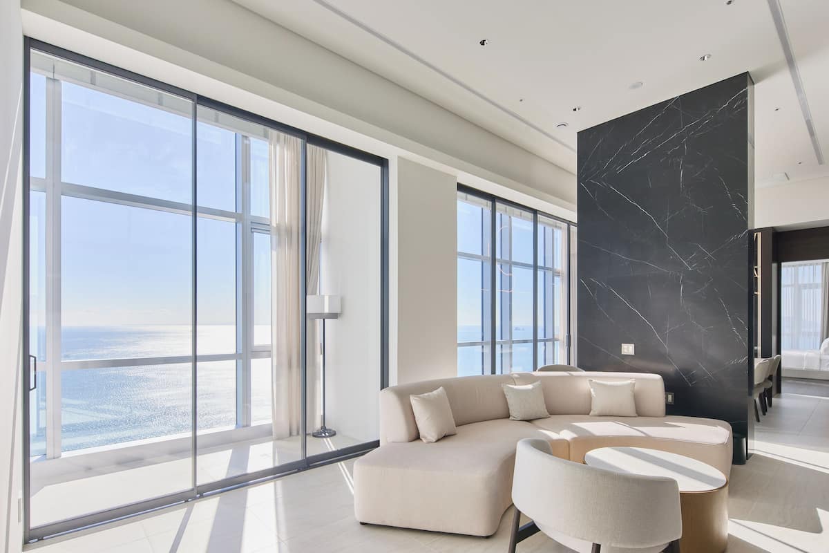 A modern living room with large windows, a sectional sofa, and a marble accent wall.