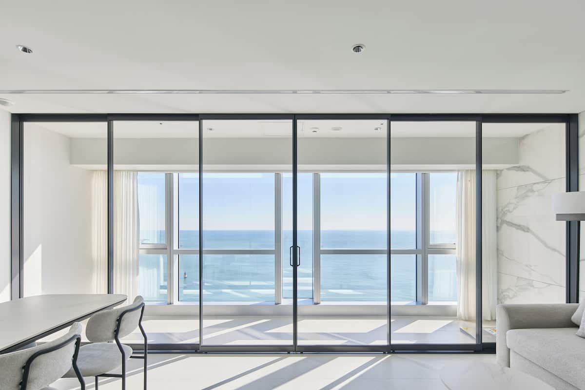 A modern room with a large sliding glass door leading to a balcony with a view of the sea.